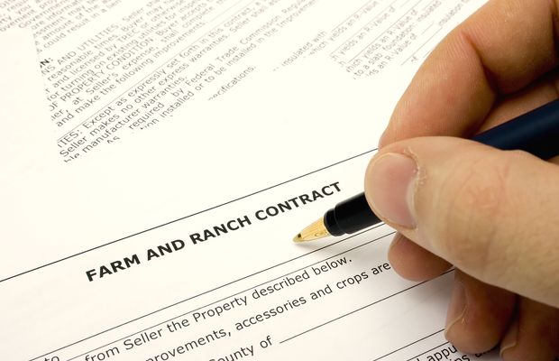 A hand signing a farm and ranch sale contract