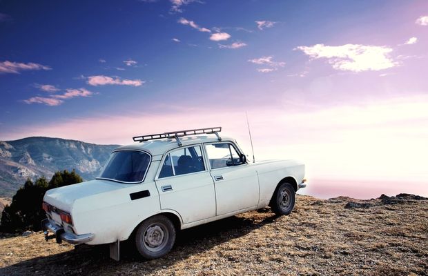 An old car with a roof rack parked on bare rock above a valley