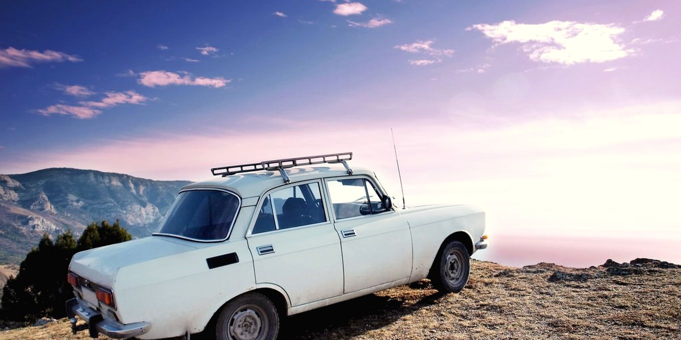 An old car with a roof rack parked on bare rock above a valley