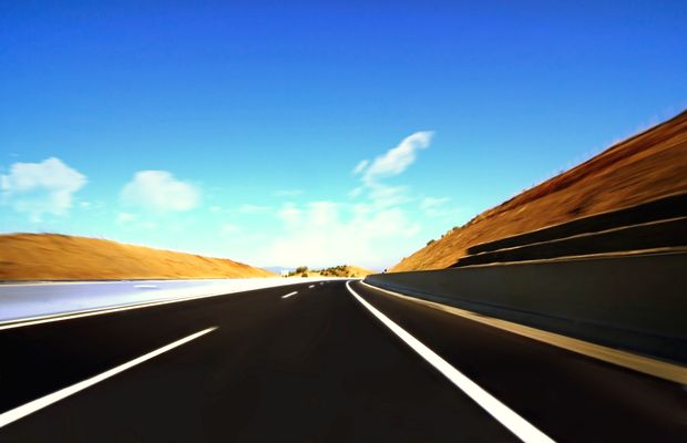 A highway curving past a bare reddish hillside