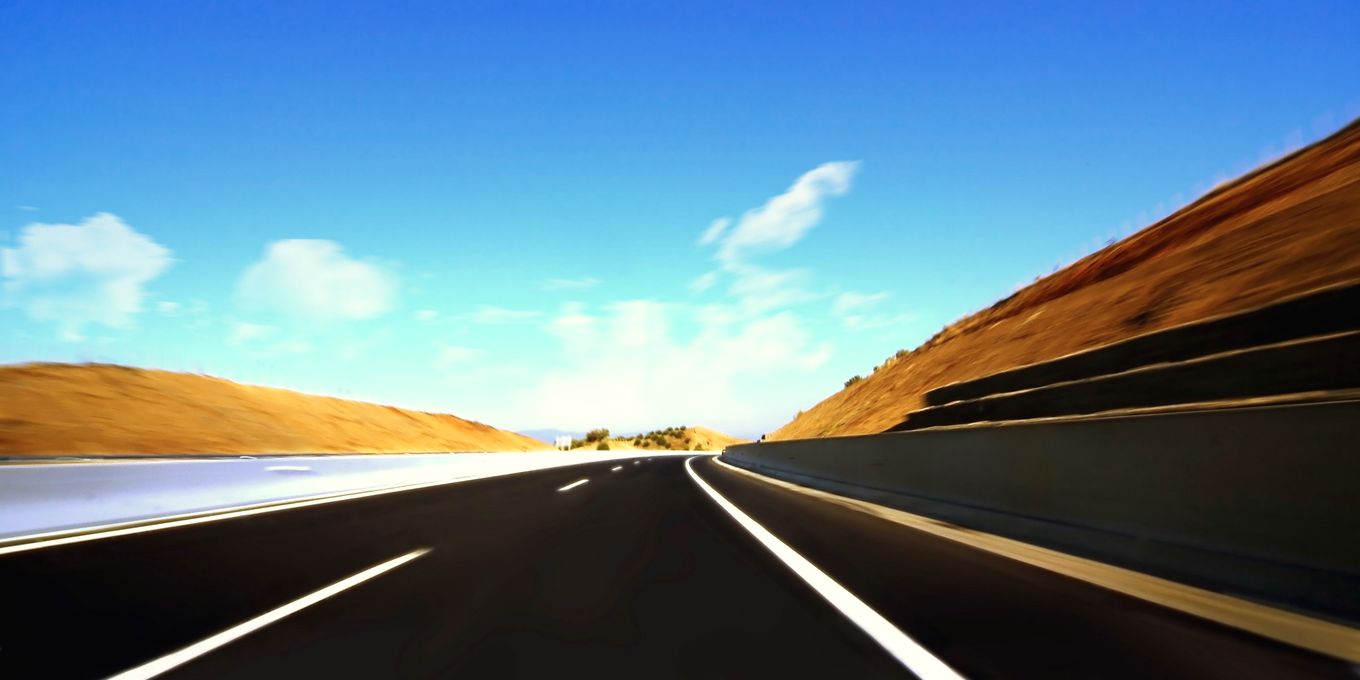 A highway curving past a bare reddish hillside