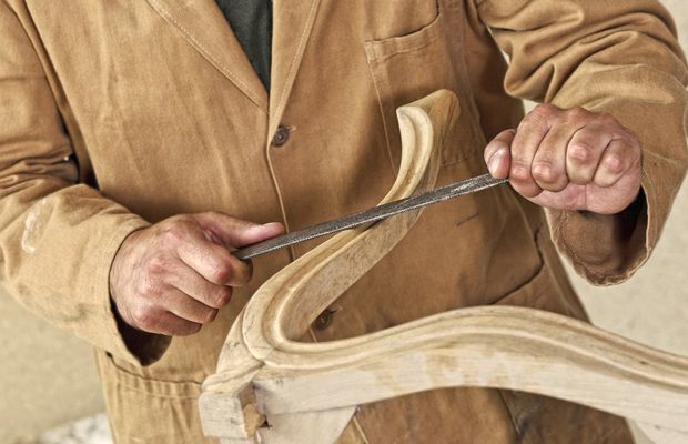 Hands carving a curved piece of pale wood with a chisel