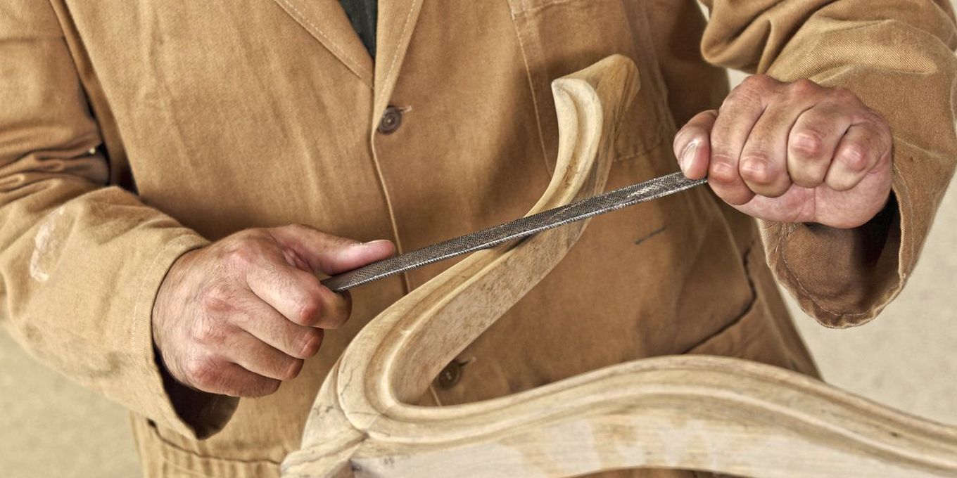 Hands carving a curved piece of pale wood with a chisel