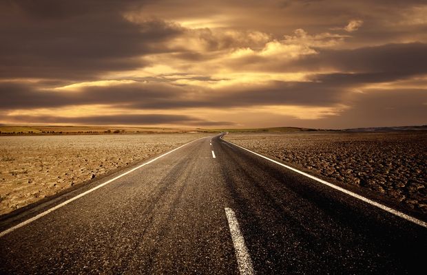 An empty two-lane road running toward a sunset over dry country
