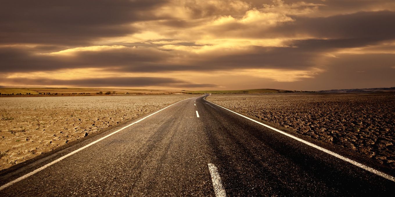 An empty two-lane road running toward a sunset over dry country